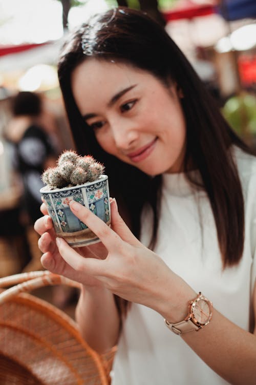 Cheerful Asian woman with small potted cactus in market
