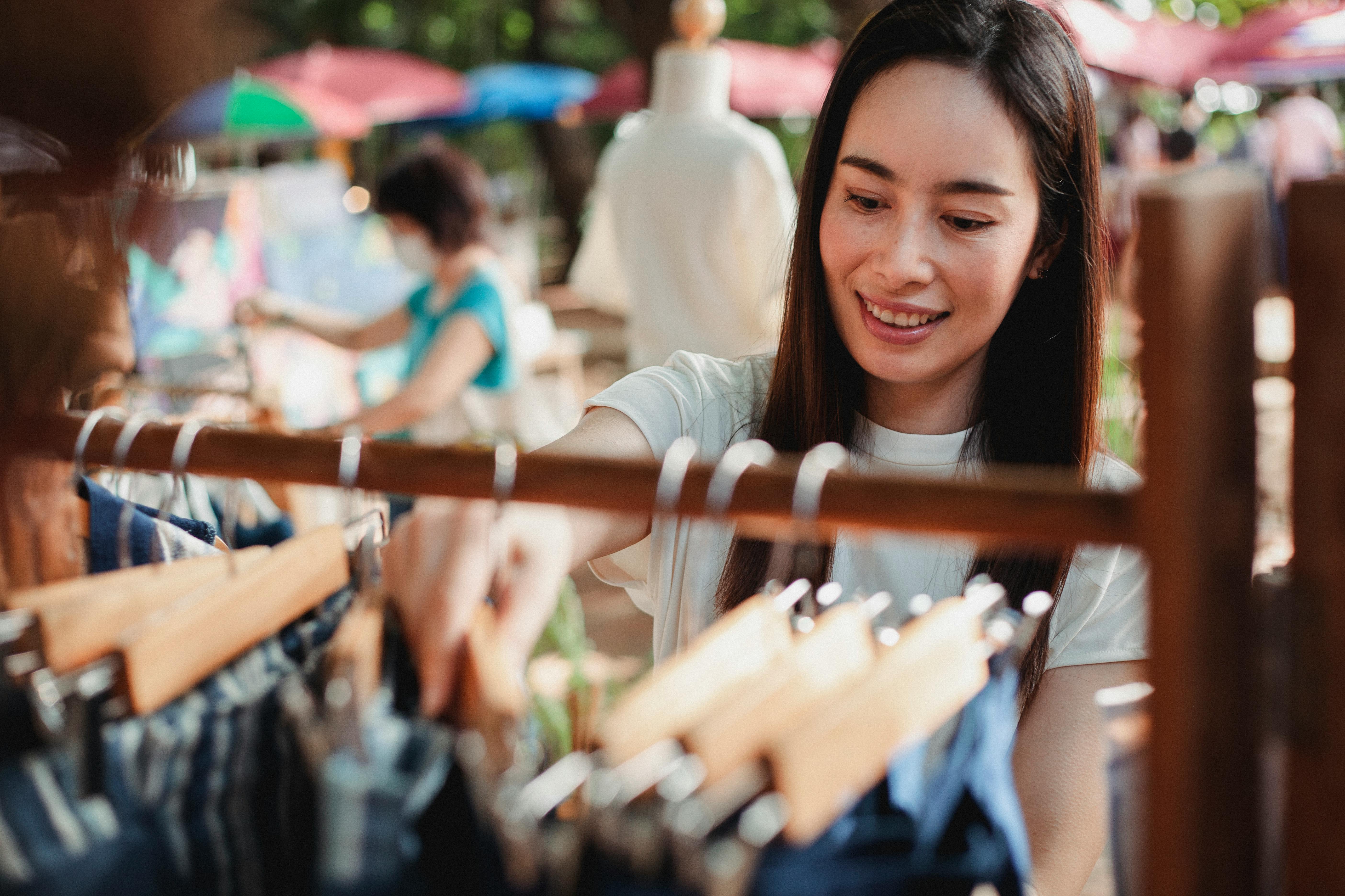 亚洲女人喜欢微笑着在户外市场浏览衣架购物