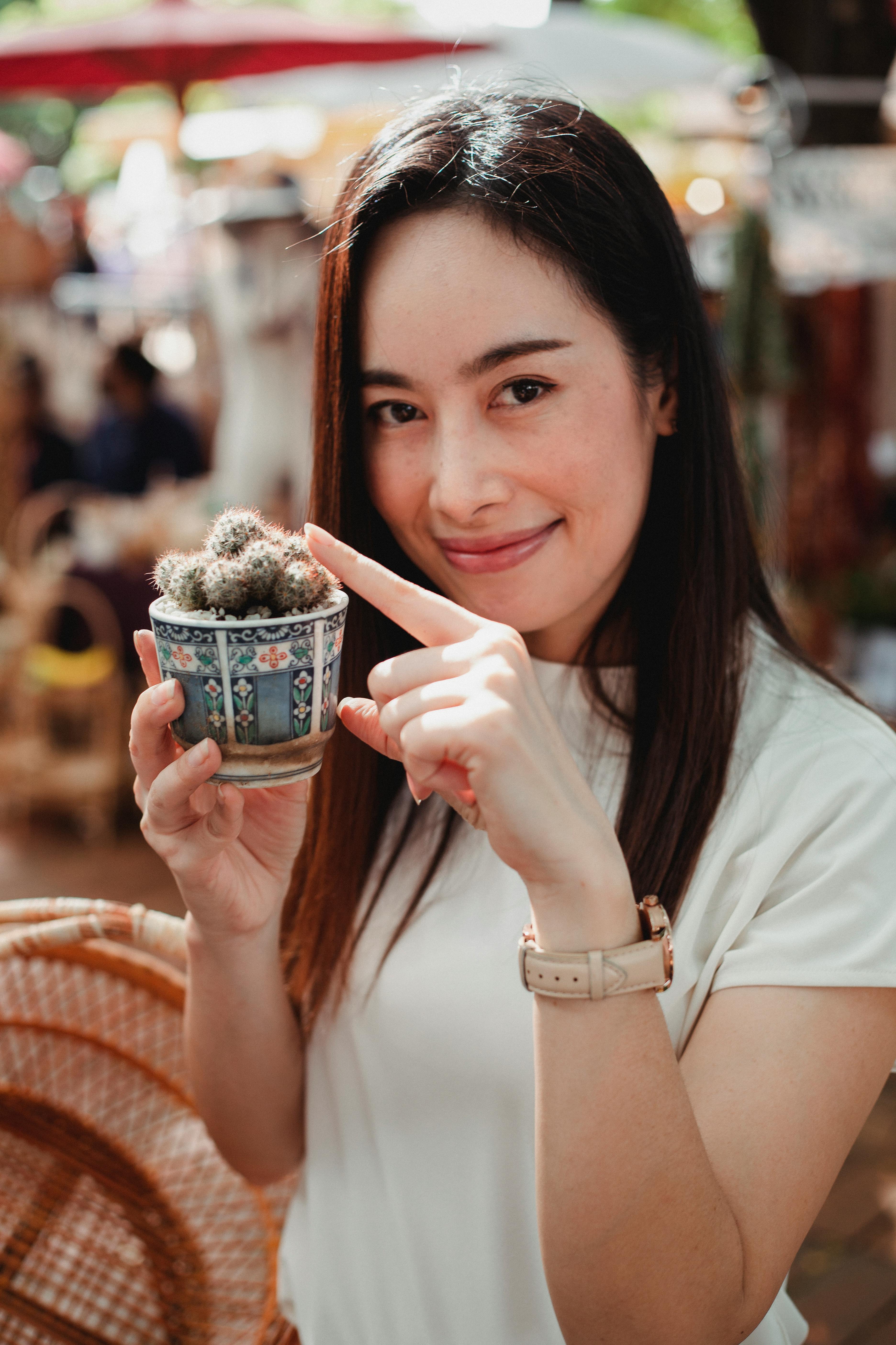 glad asian woman holding small cactus in street market