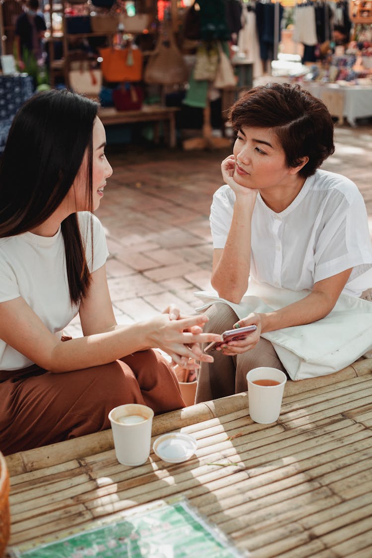 Positive Asian Women Chatting And Having Coffee In Outdoor Cafe