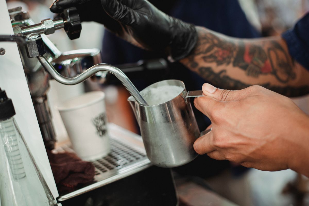 Real barista holding a milk pitcher under an espresso machine steam wand