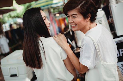 Joyful Asian women laughing while ordering drink in outdoor cafe