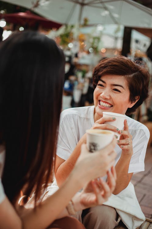 무료 야외 카페테리아에서 커피를 마시는 쾌활 한 아시아 여성 스톡 사진