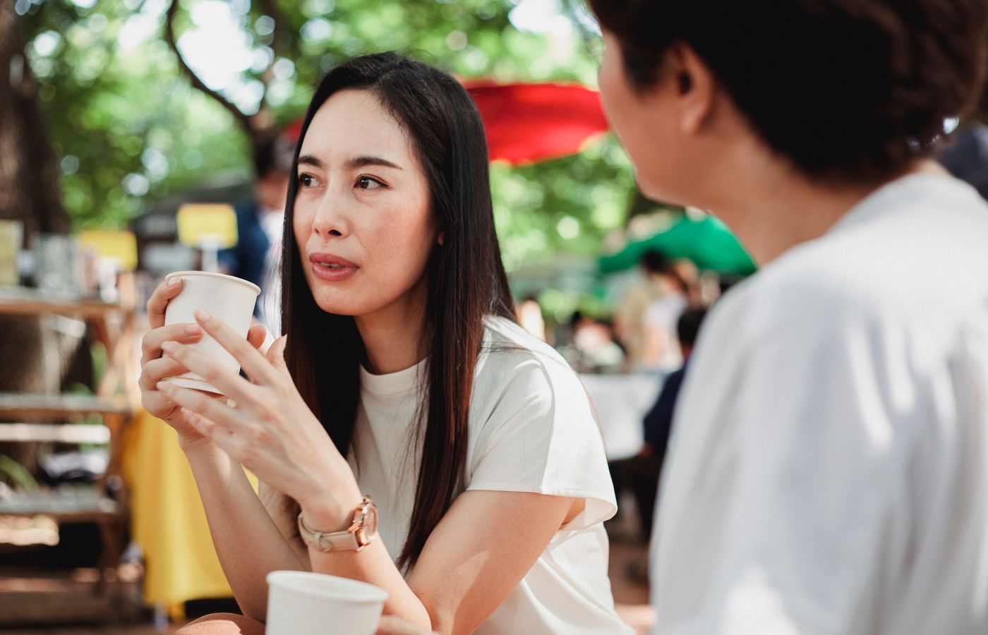 Two women enjoying a coffee together in a sunny outdoor setting, engaging in friendly conversation.