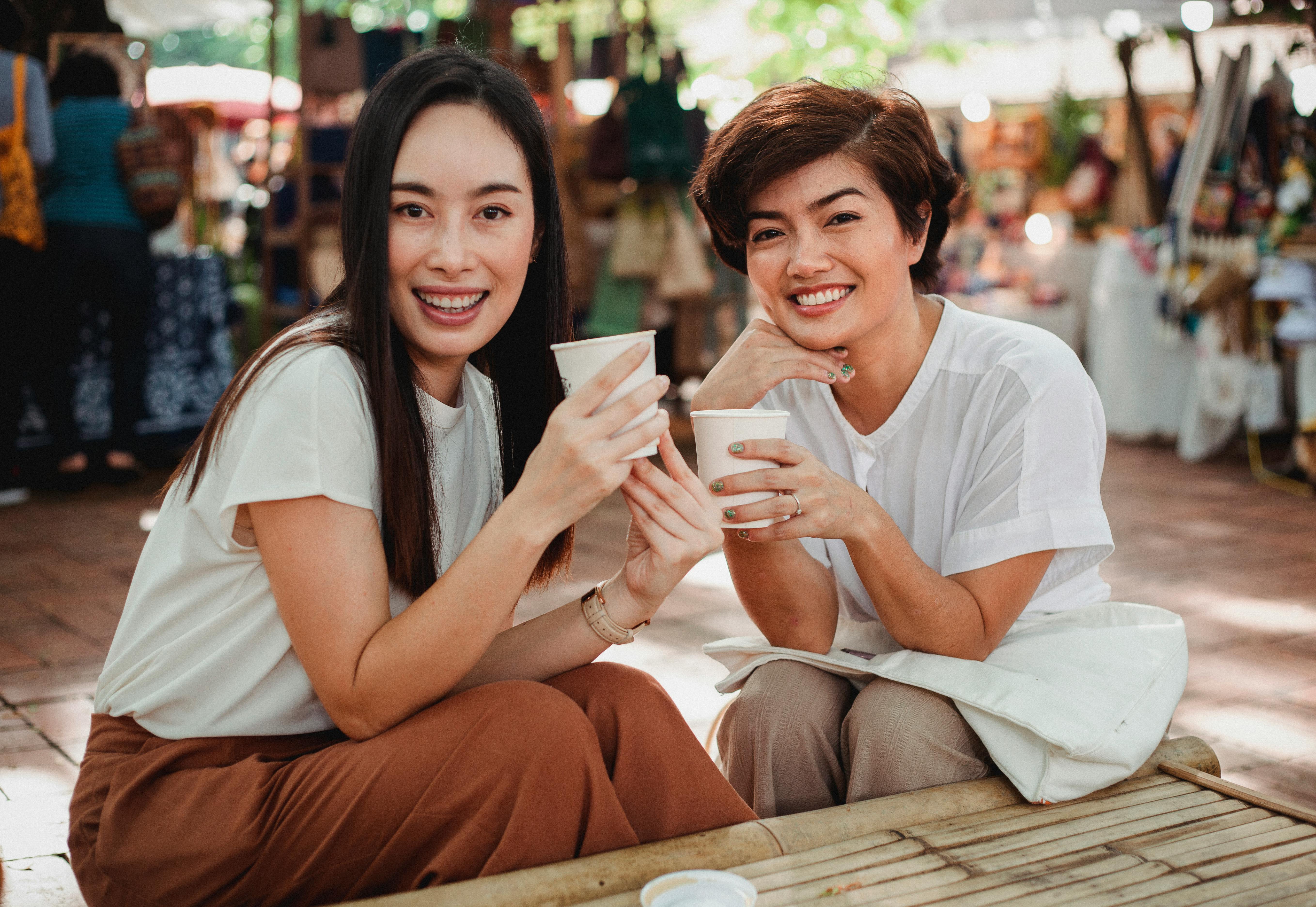 pretty asian women with takeaway coffees sitting in outdoor cafe