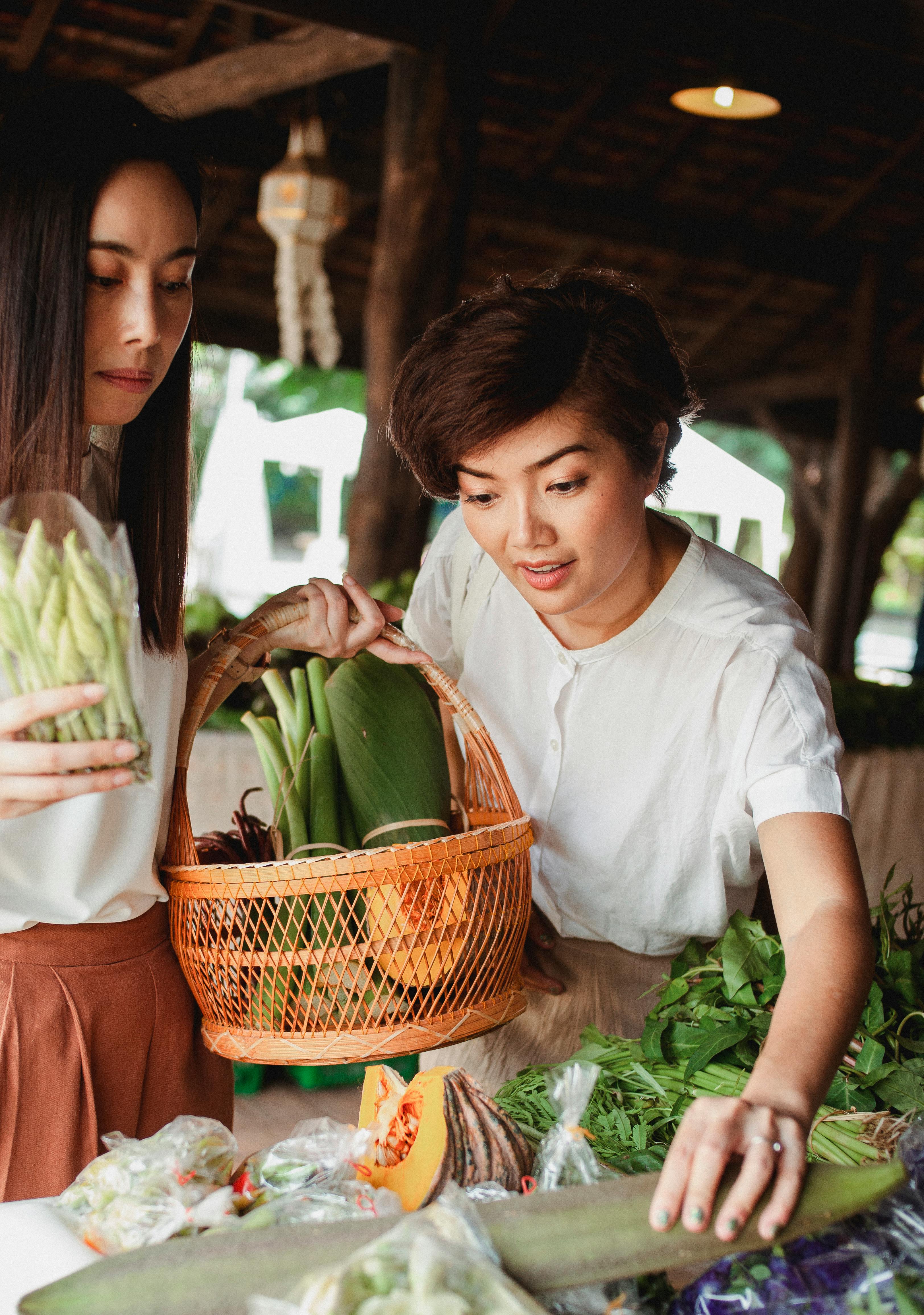 crop asian girlfriends choosing fresh vegetables on counter in market