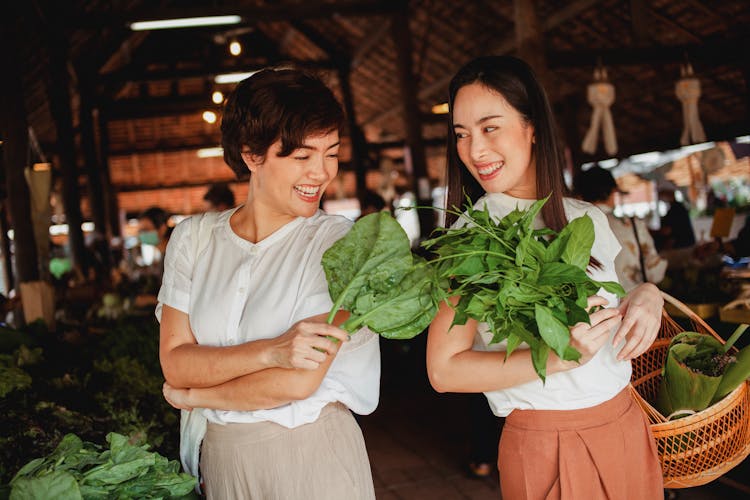 Glad Asian Buyers With Fresh Green Herbs In Bazaar