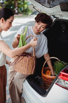 年轻的少数民族妇女把柳条篮和蔬菜放在镇上的汽车后备箱里