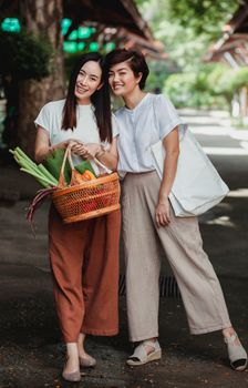 两名妇女带着柳条篮和新鲜蔬菜，在户外购物时微笑着