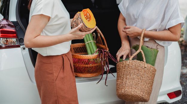 两名妇女把有机蔬菜从汽车上卸下来，装进柳条篮里