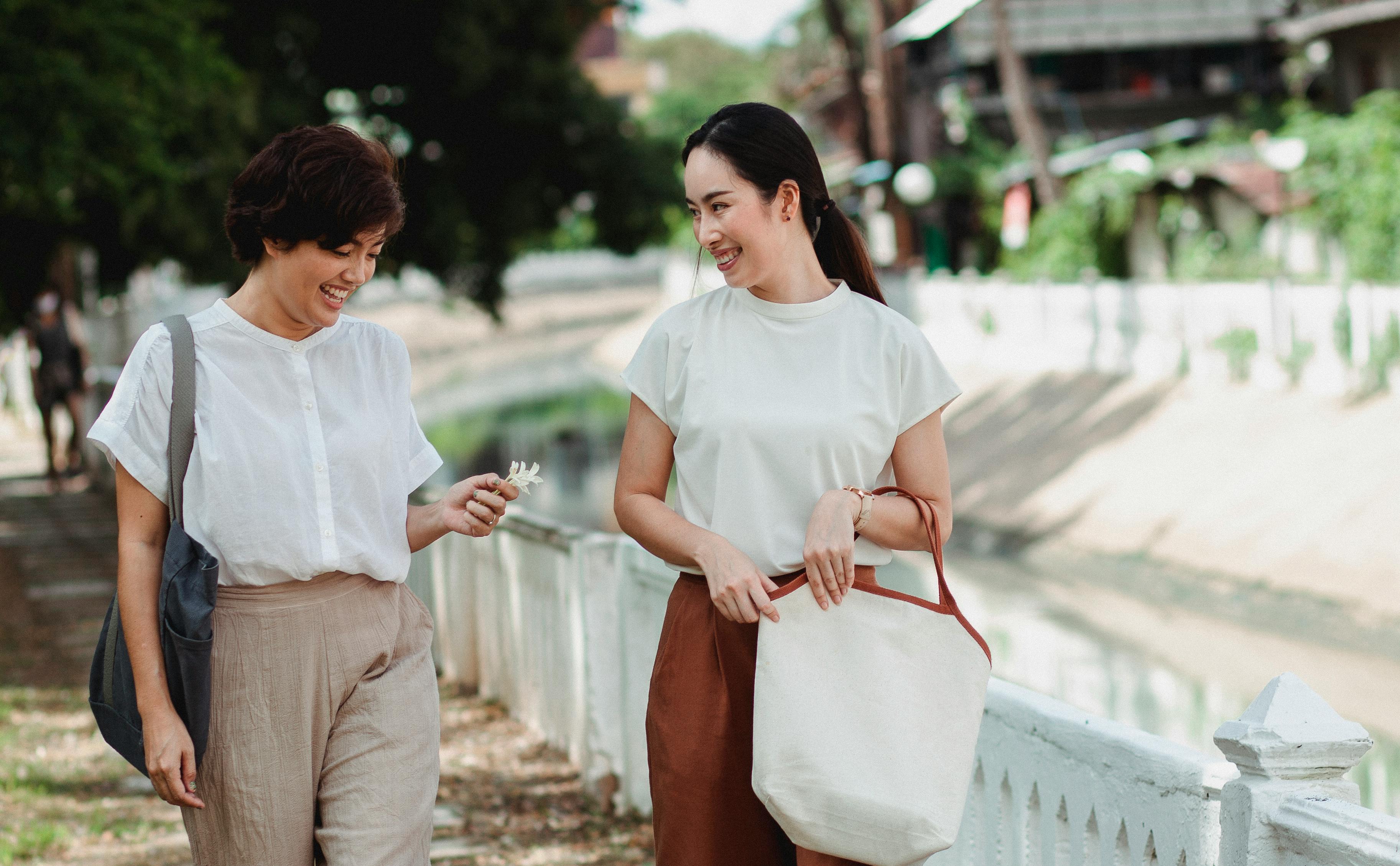 happy asian girlfriends talking while walking on street