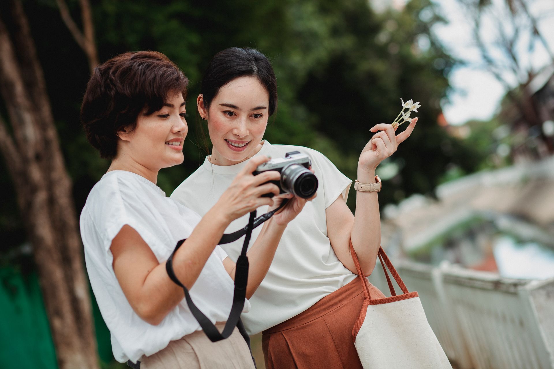 Young glad ethnic lady sharing photo camera with charming female partner on city street in summer