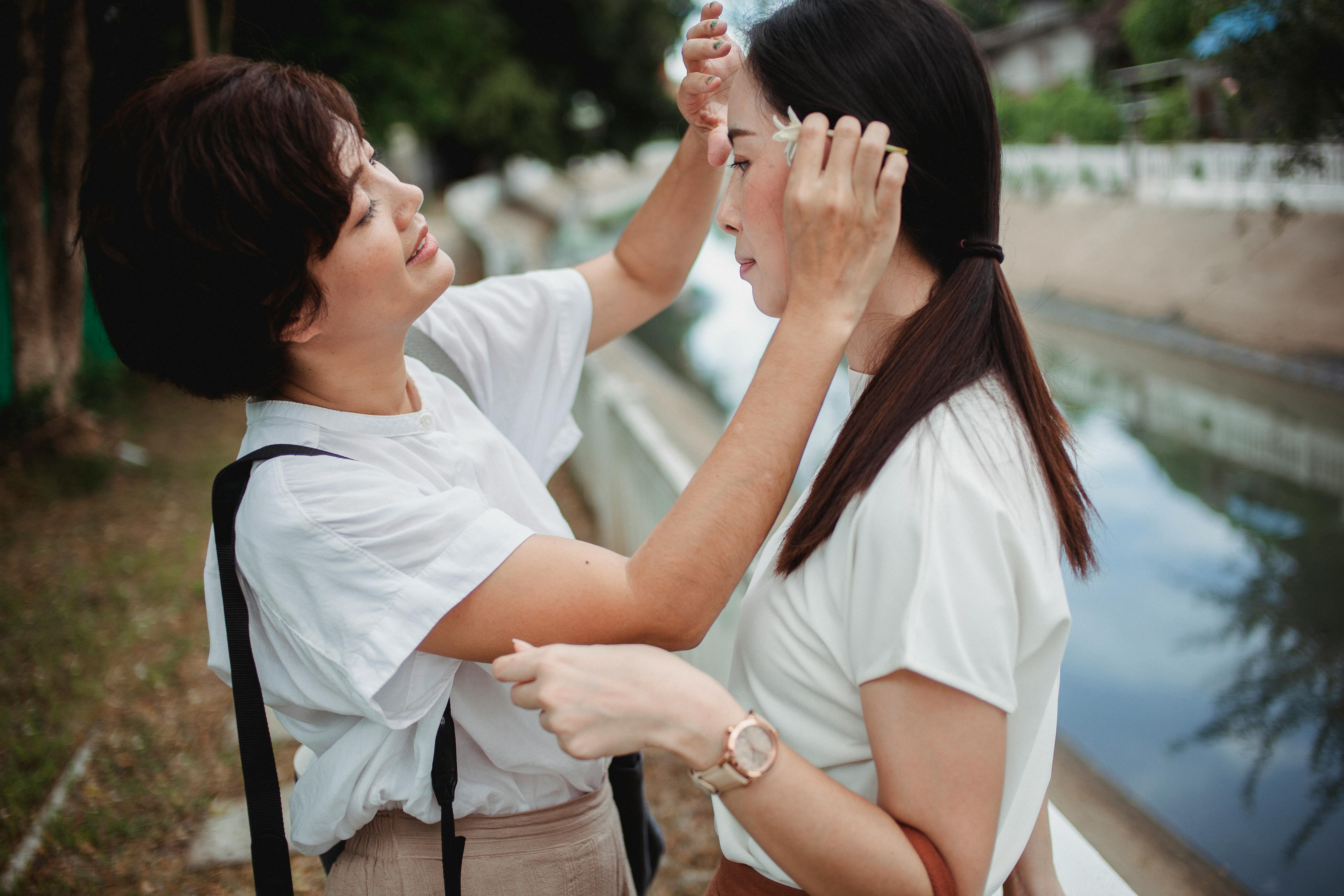 smiling asian woman touching forehead of homosexual partner on embankment