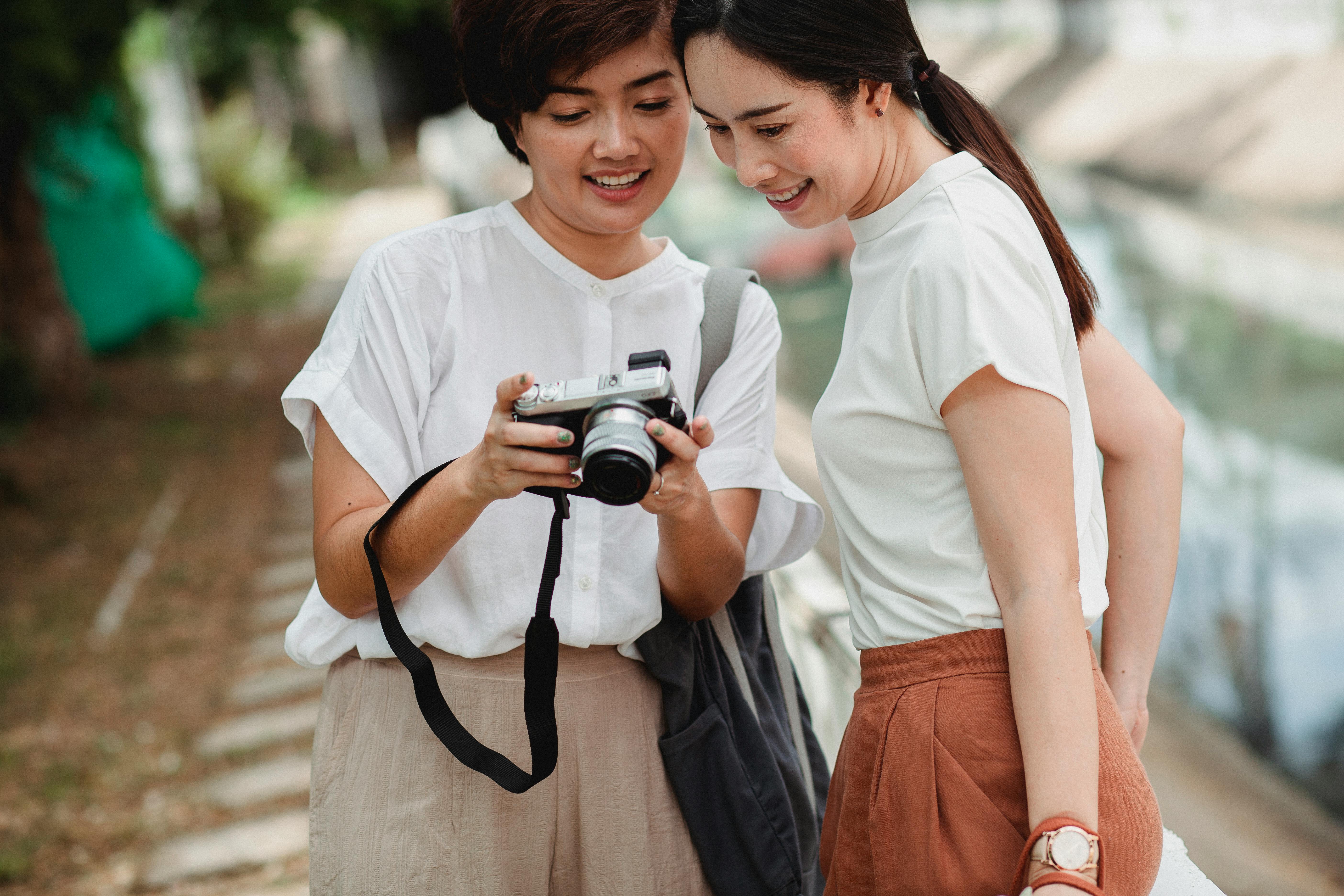 Crop happy Asian girlfriends sharing photo camera on city street · Free  Stock Photo