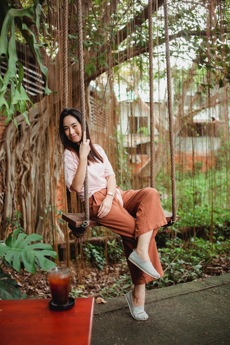 Smiling Asian Woman On Swing In City Park