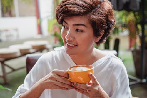 Улыбается азиатская женщина, пьющая чашку кофе