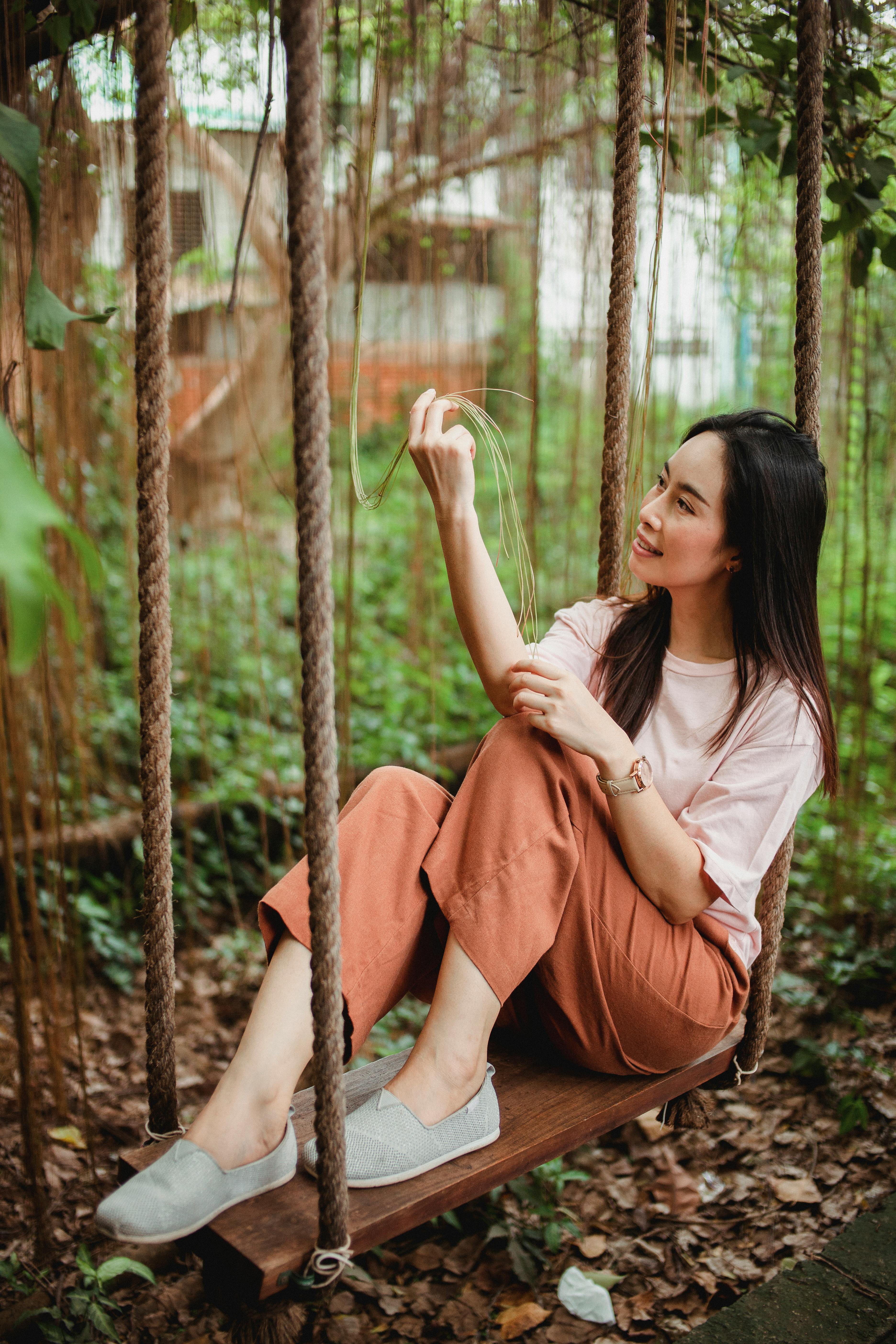 cheerful asian female resting on swings in garden