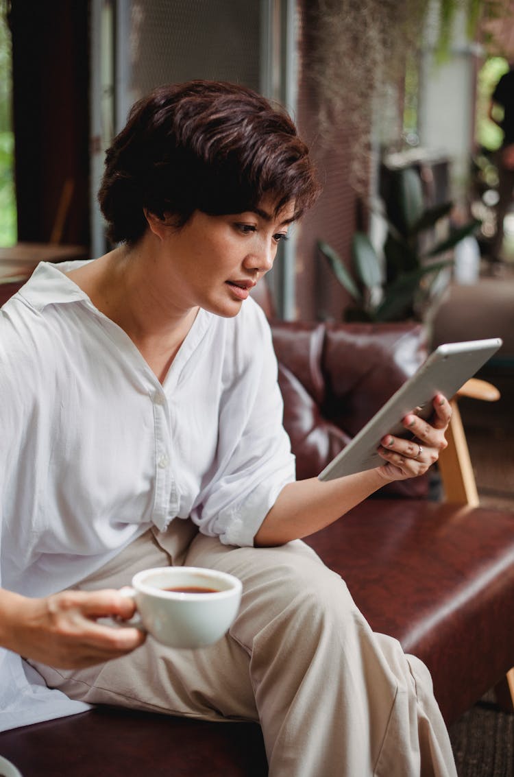 Focused Asian Woman Using Tablet And Drinking Coffee