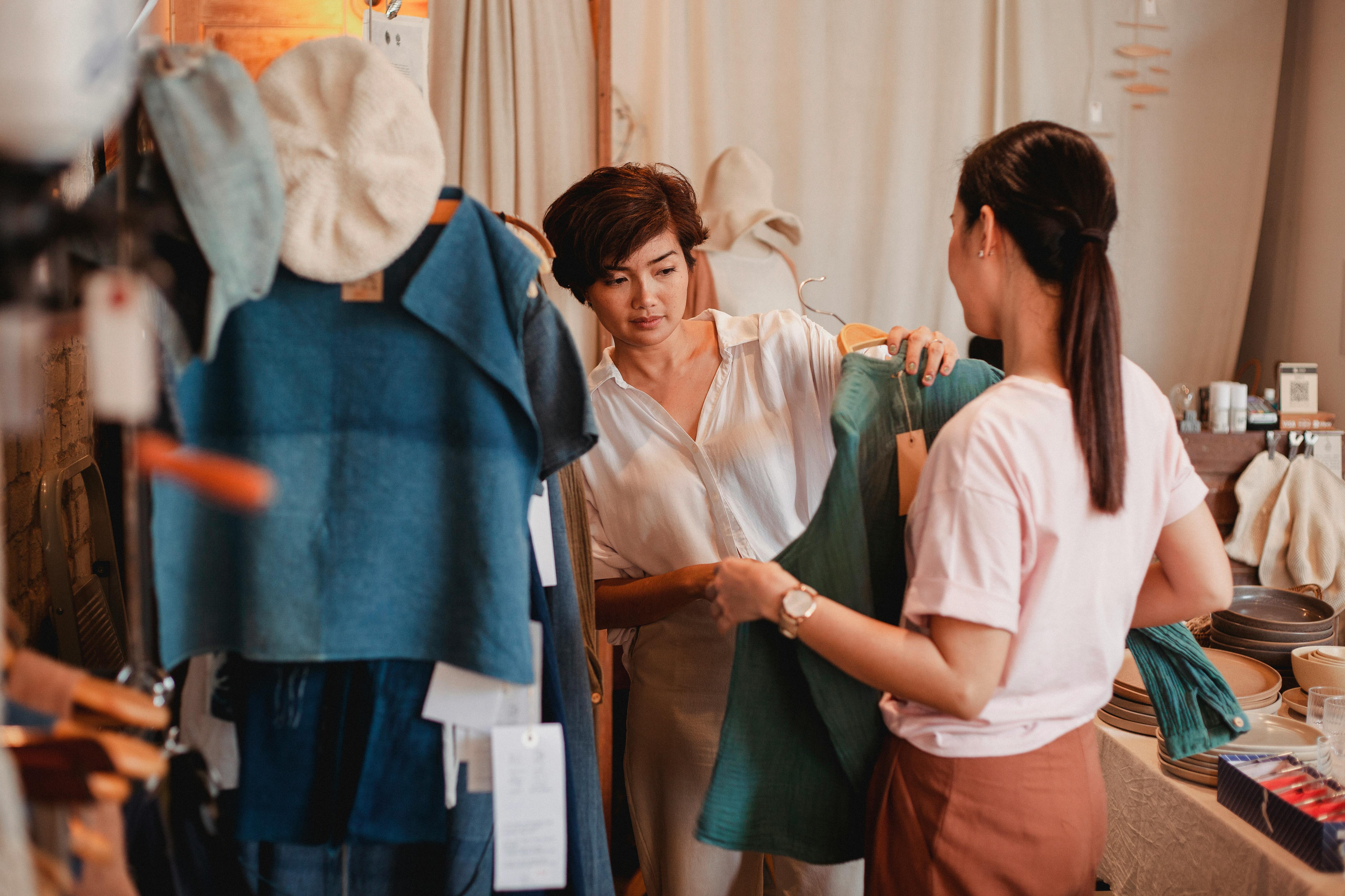 unrecognizable shopper with asian girlfriend choosing clothes in shop