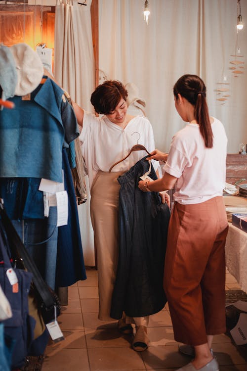 Free Asian shopper with anonymous partner choosing skirt in clothing store Stock Photo