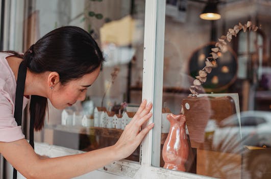 Side view of young ethnic female leaning forward while touching glass wall of store in town