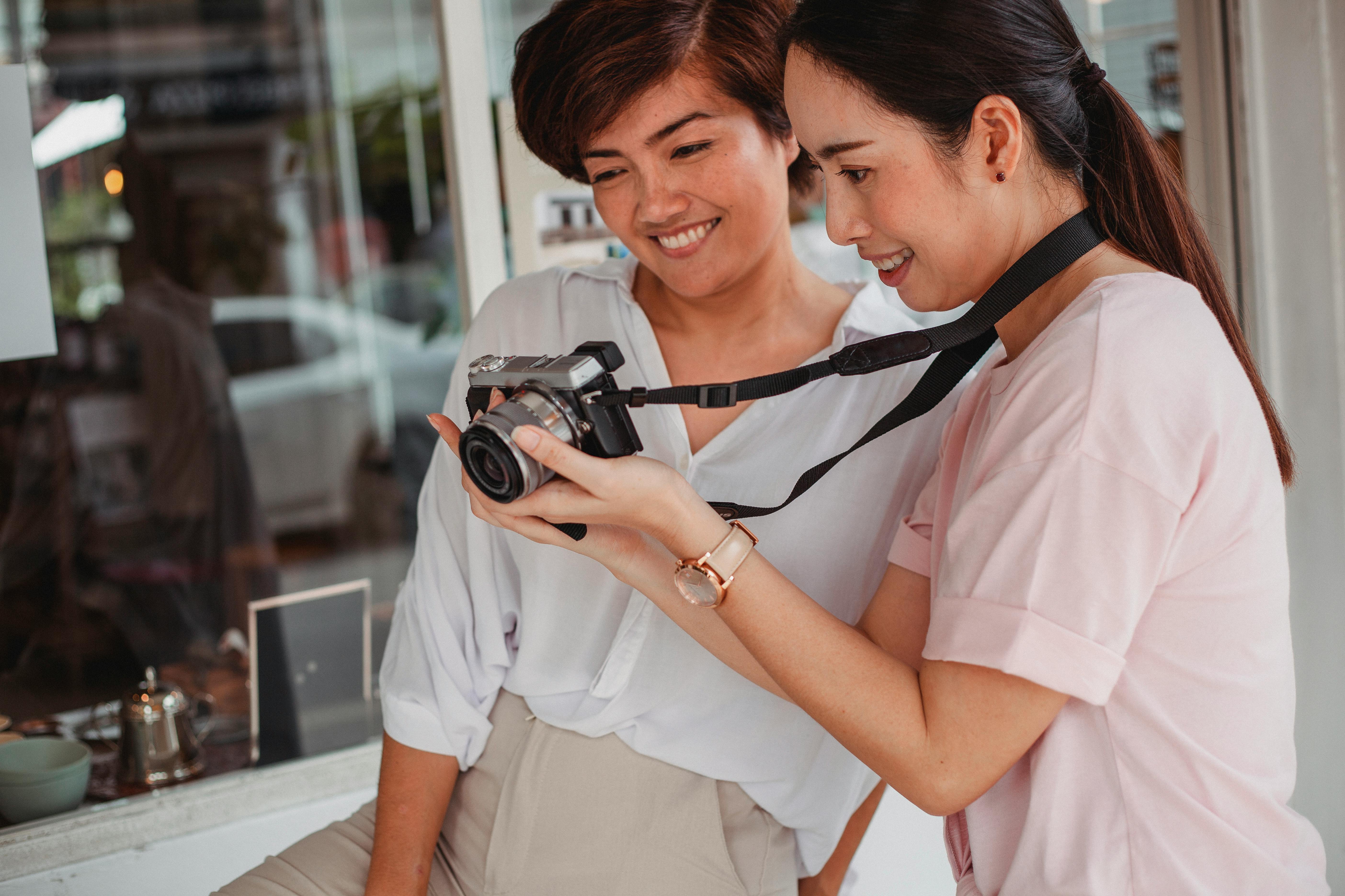 crop happy asian girlfriends sharing photo camera on city street