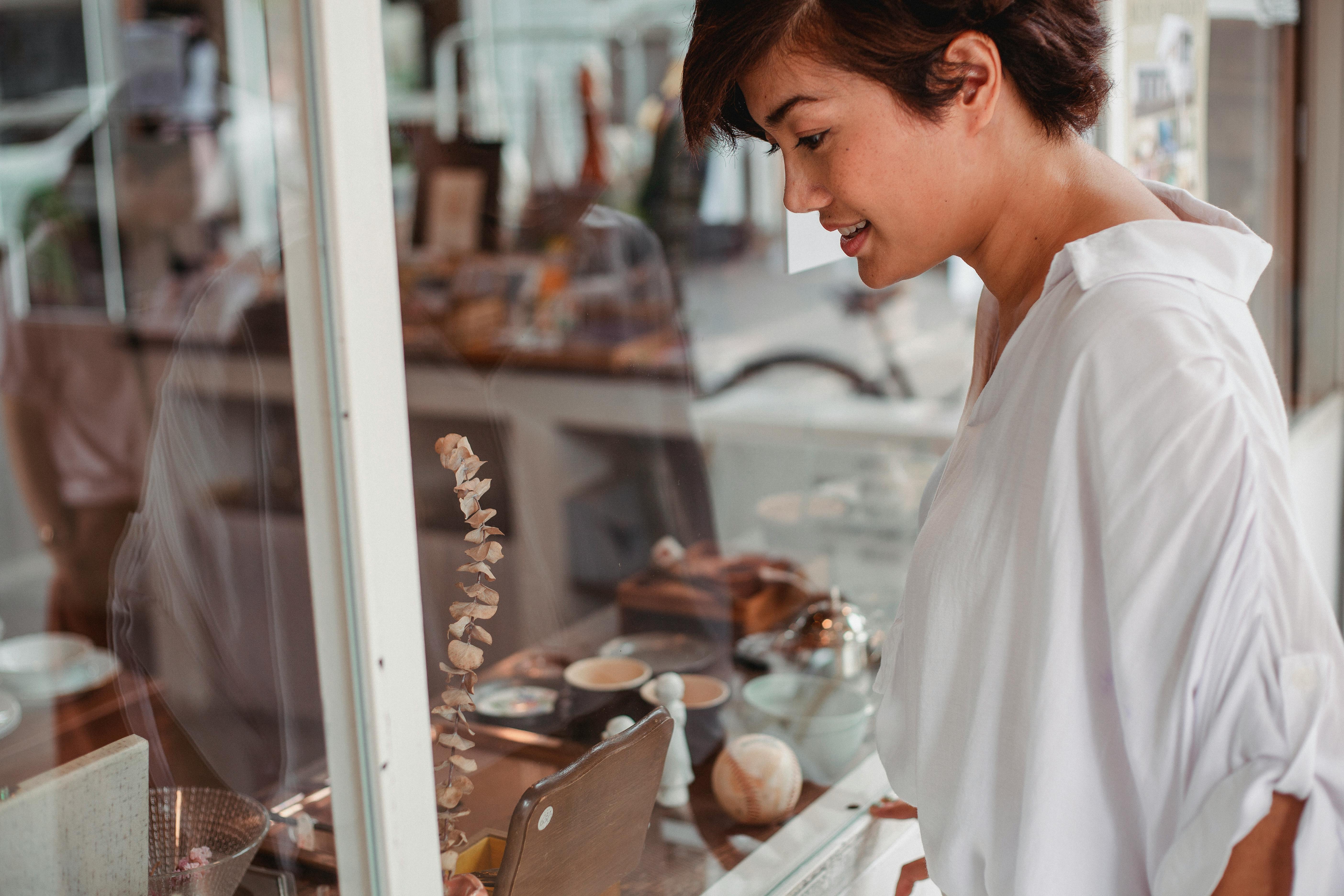 Free Side view of crop young smiling ethnic female watching assortment of store through glass wall in city Stock Photo