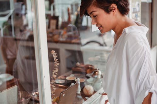 Free Side view of crop young smiling ethnic female watching assortment of store through glass wall in city Stock Photo