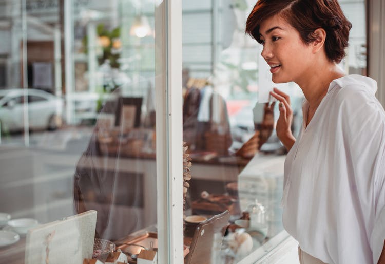 Crop Asian Woman Watching Shop Items Through Showcase On Street