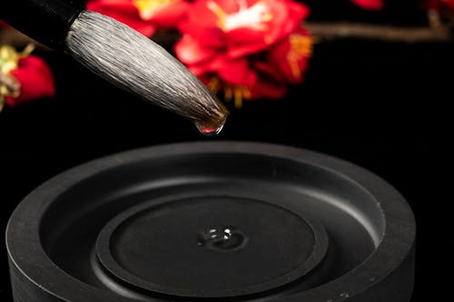 Calligraphy brush pen with soft pointed tip and water drip over black ink stone on table