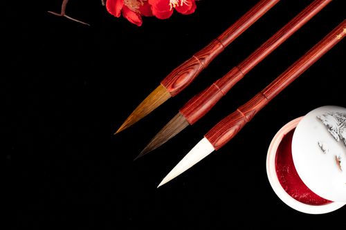 Free Overhead view of various calligraphy brush pens near decorative jar of red paint on black background Stock Photo