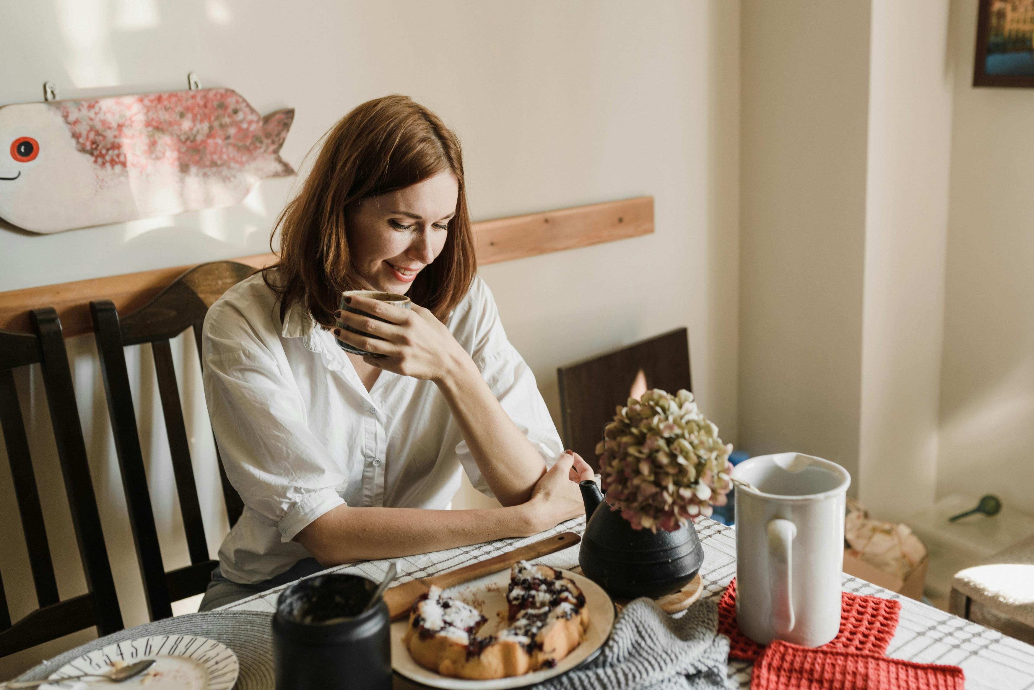 Woman enjoying a morning coffee and pastry at home, captured indoors with a warm ambiance.