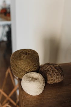Close-up of natural yarn rolls in earthy tones on a wooden surface indoors.