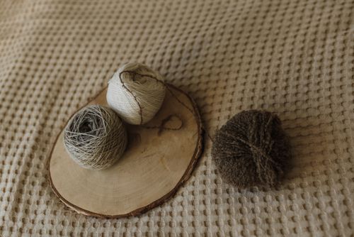 Free Close-up of natural colored yarn balls resting on a wooden tray over a textured surface. Stock Photo