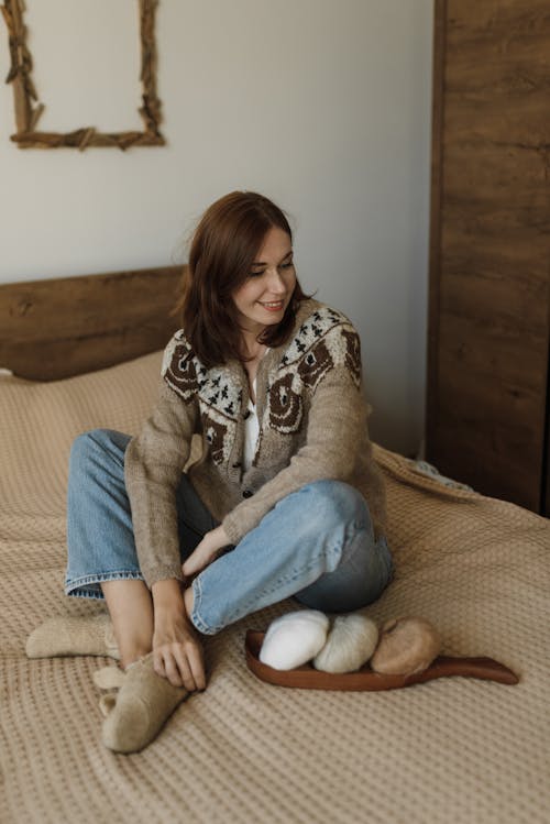 Woman in Brown Cardigan Sitting on a Bed