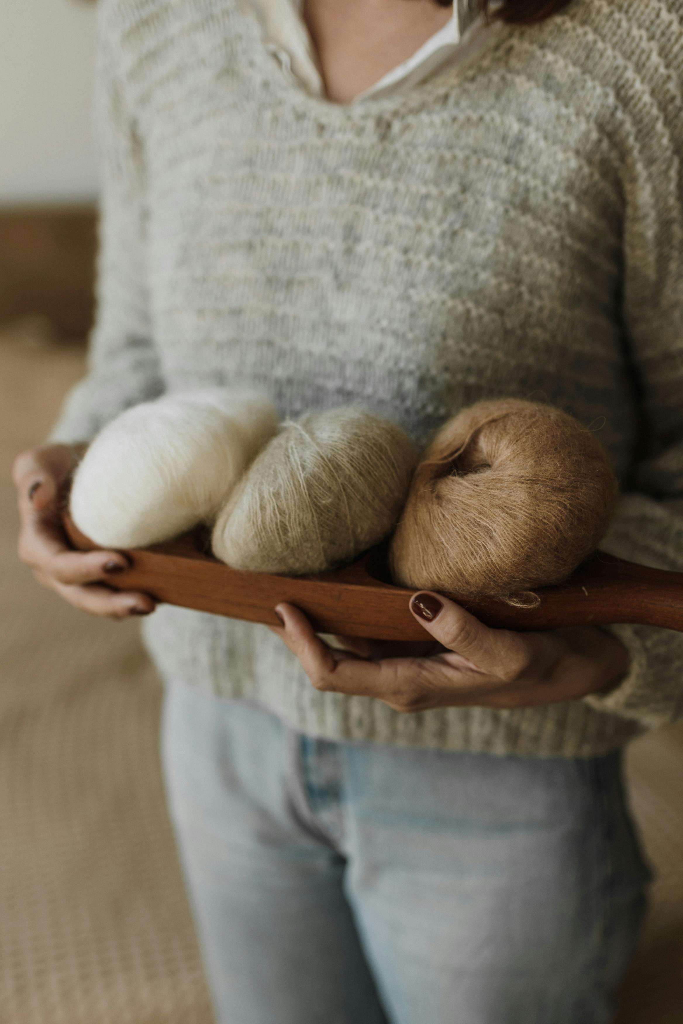 Woman holding a wooden tray with yarn rolls, wearing a cozy knitted sweater.