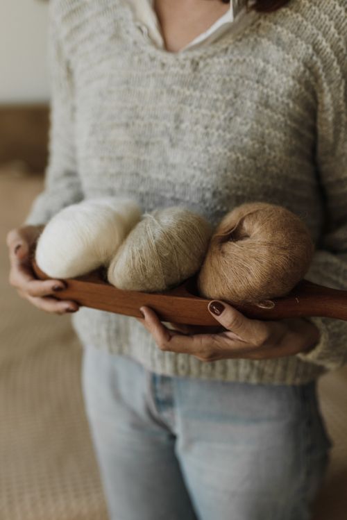 Free Woman holding a wooden tray with yarn rolls, wearing a cozy knitted sweater. Stock Photo