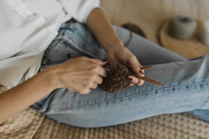 A person in denim knitting with brown yarn