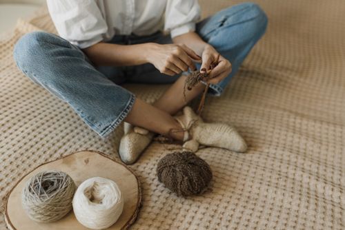 Free Person knitting with yarn rolls and needles inside a cozy home setting. Stock Photo