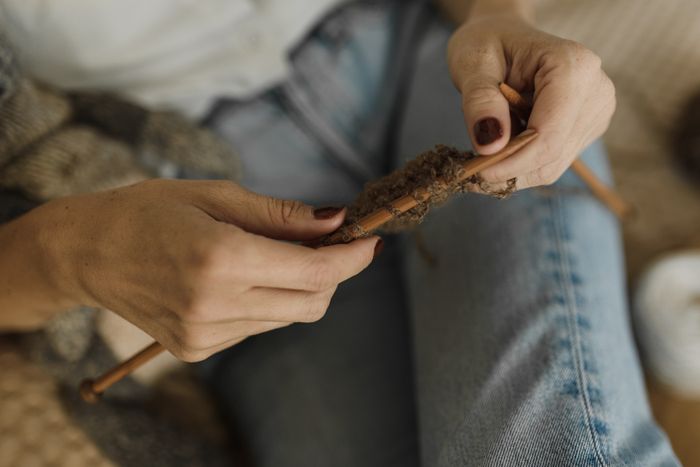 Close-up of hands knitting with brown yarn and wooden needles