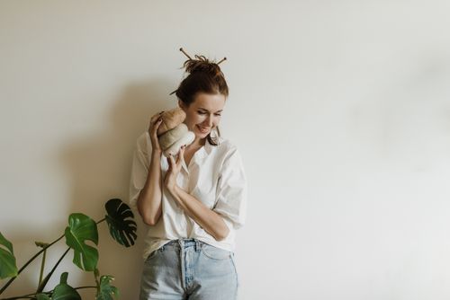 Free Young woman smiling indoors holding yarn rolls against a white background. Stock Photo