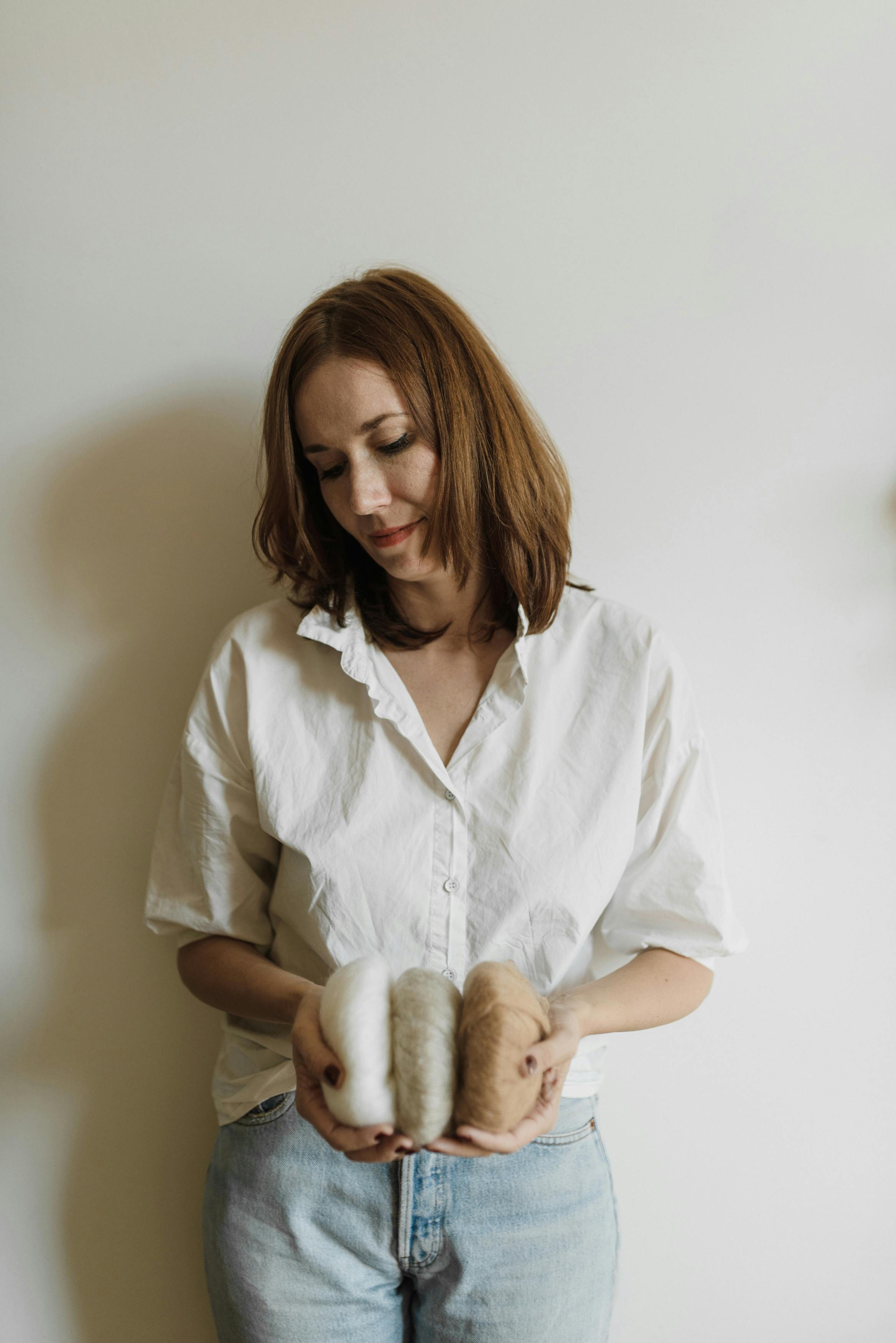 A woman in a white shirt holding soft yarn rolls, evoking warmth and creativity indoors.