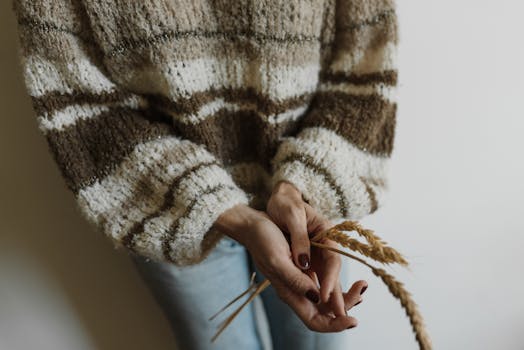 Close-up of hands holding wheat stalks against a knit sweater, highlighting texture and natural elements.