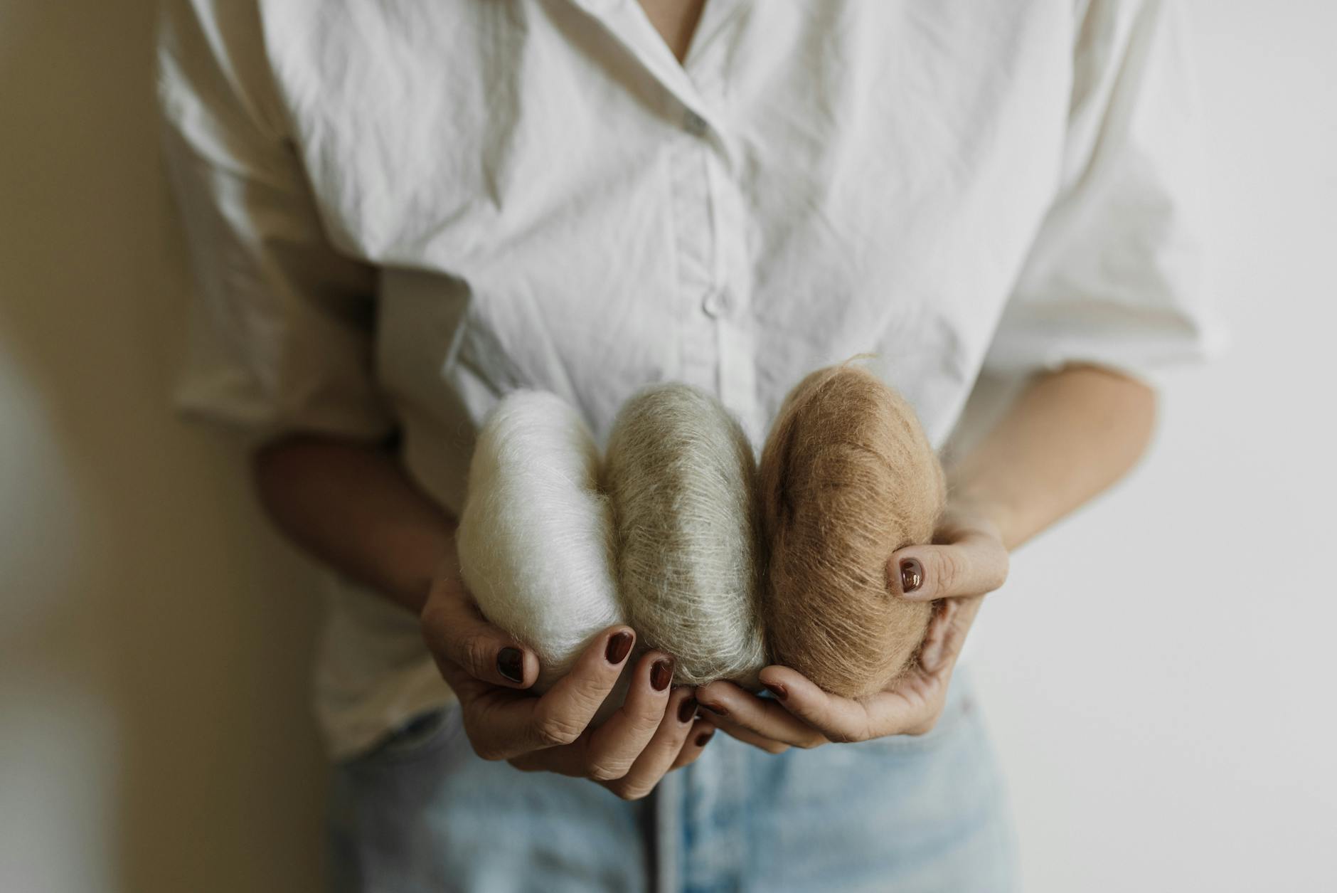 Hands holding three yarn rolls in neutral shades, perfect for knitting projects.