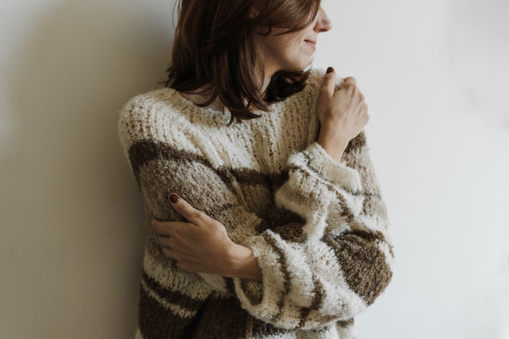 A woman in a knit sweater hugging herself with a calm expression