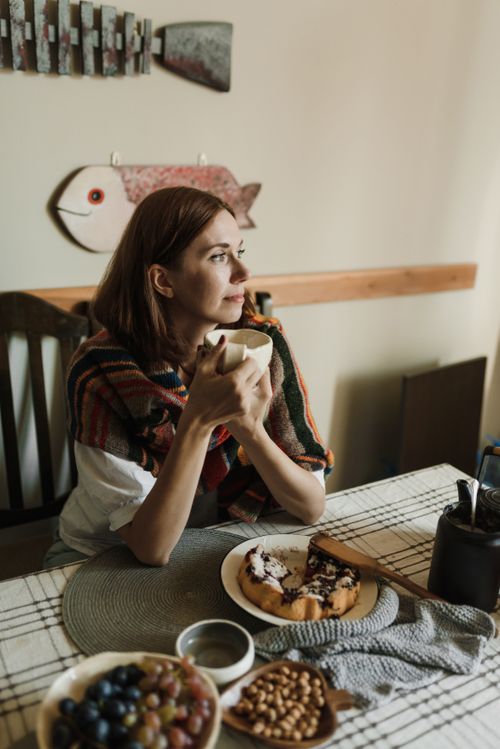 Free A woman in a cozy setting enjoys breakfast with coffee, cake, and fruit. Stock Photo