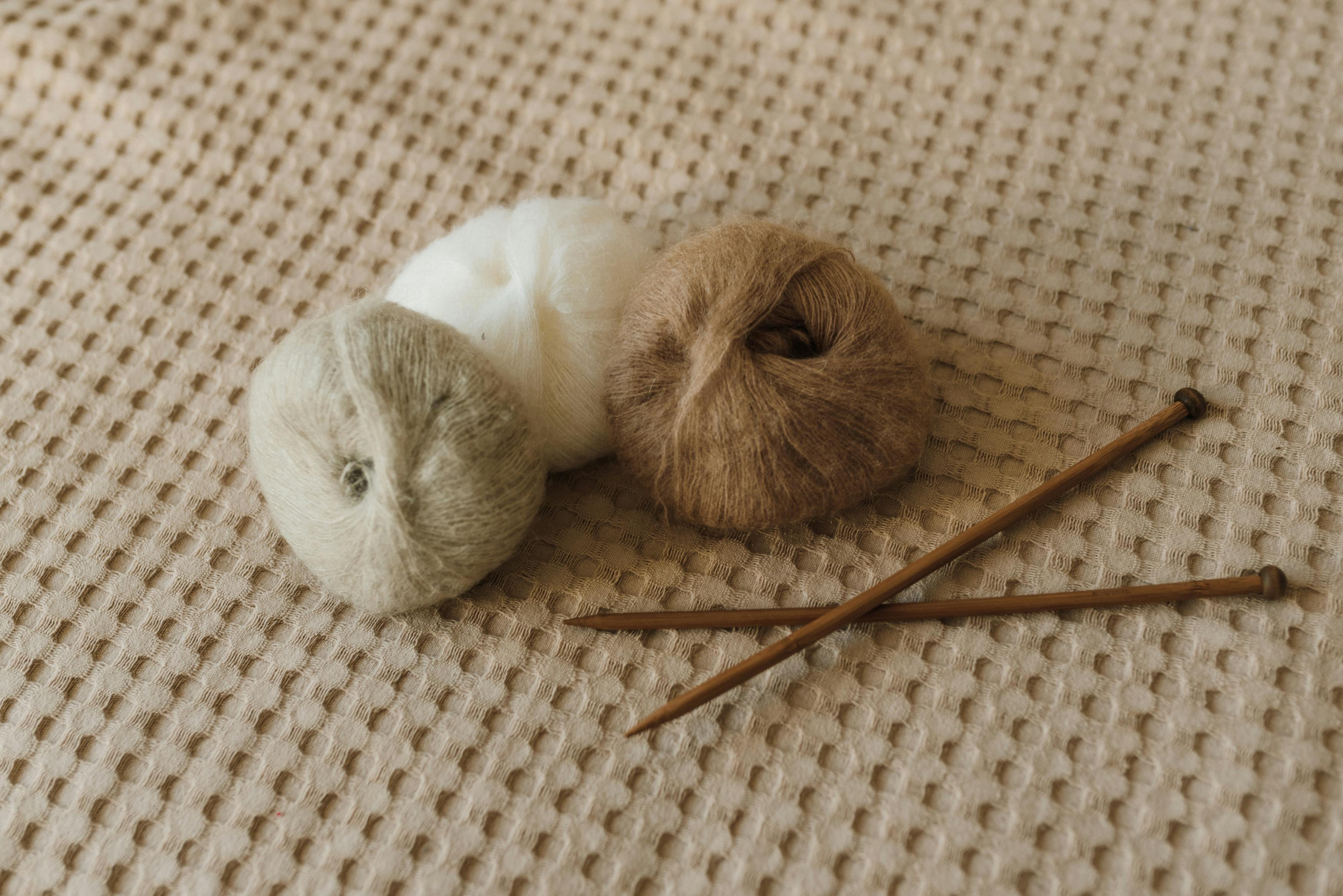 Warm and inviting still life of yarn rolls and knitting needles on a textured fabric surface.