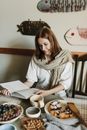 From above of positive female reading book while having tea with pie and fruits at table
