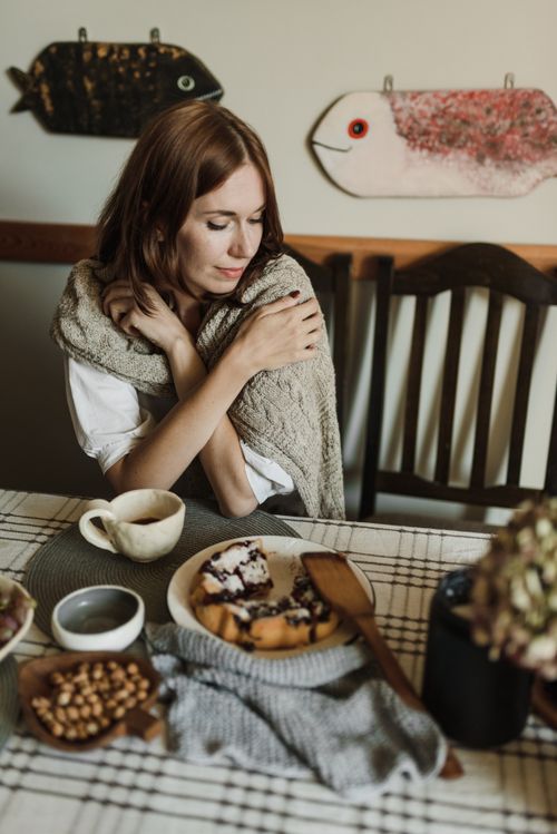Free Woman wrapped in shawl enjoying coffee and slice of cake at a dining table. Stock Photo