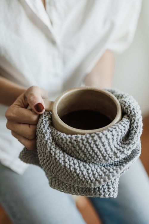 Free Warm coffee in a neutral mug held by a person wrapped in a knitted cloth for a cozy vibe. Stock Photo